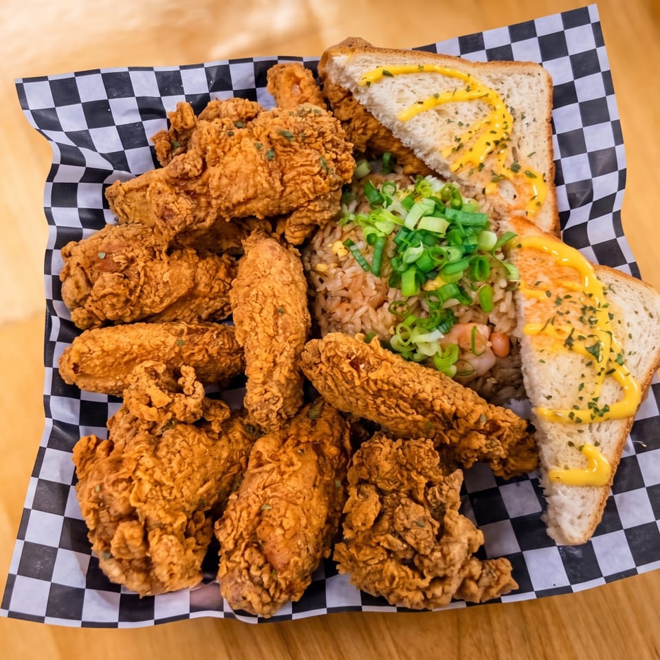 Crispy fried chicken pieces, rice with green onions, and toasted bread on checkered paper.