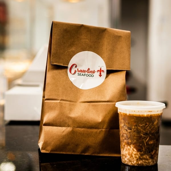 Crawlin's Seafood takeout bag and a container of gumbo on a dark counter.