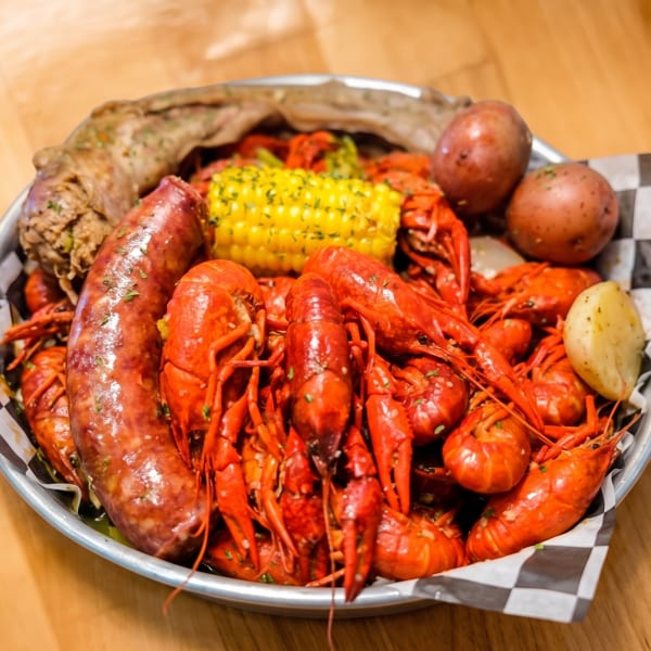A metal platter filled with red crawfish, corn on the cob, potatoes, and sausage on a wooden table.