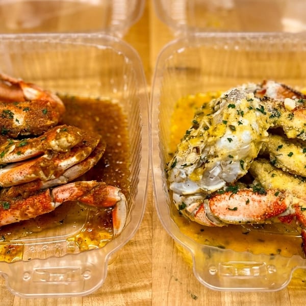 Two plastic containers filled with seasoned crab legs, one with a dark sauce and the other with a yellow sauce.