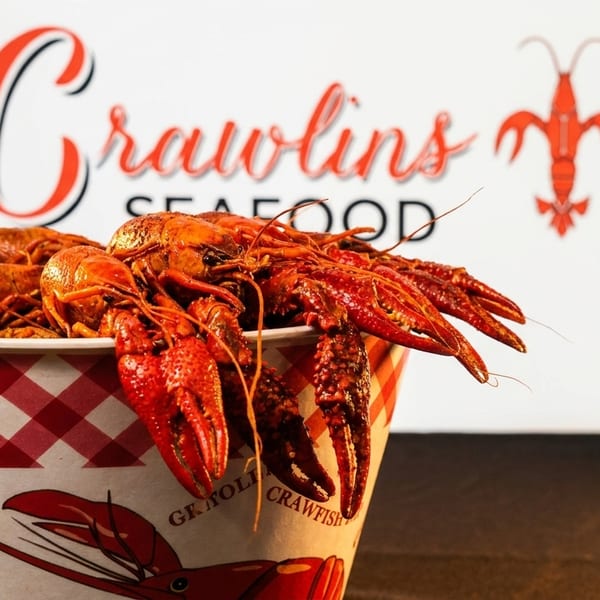 A bucket of bright red crawfish sits in front of the Crawlins Seafood logo.